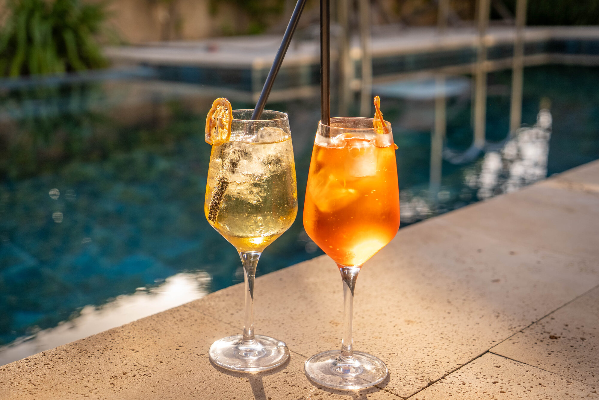 Two cocktails on the stone edge of the NEMA pool in afternoon sun